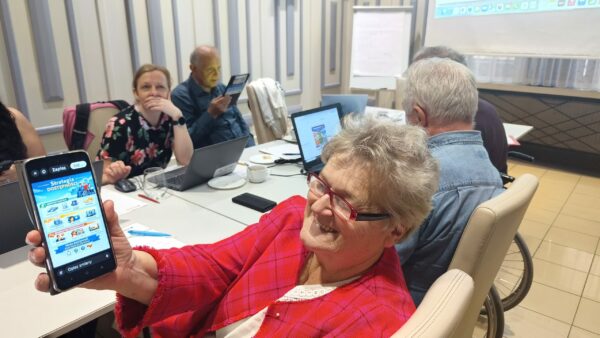 grupa uczestników szkolenia siedzi przy stołach z laptopami,