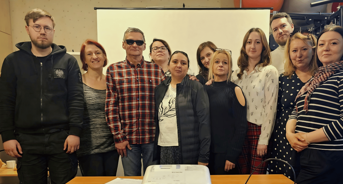 Kilku uczestników szkolenia wraz z trenerem stoi przed ekranem i pozuje do zdjecia