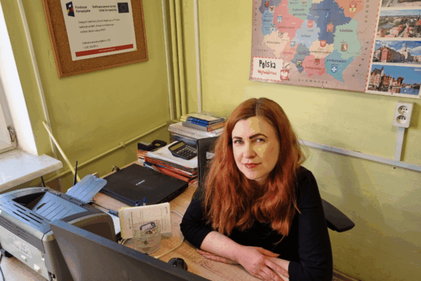 zdjęcie przedstawia kobietę siedzącą w biurze, przy biurku przed komputerem.