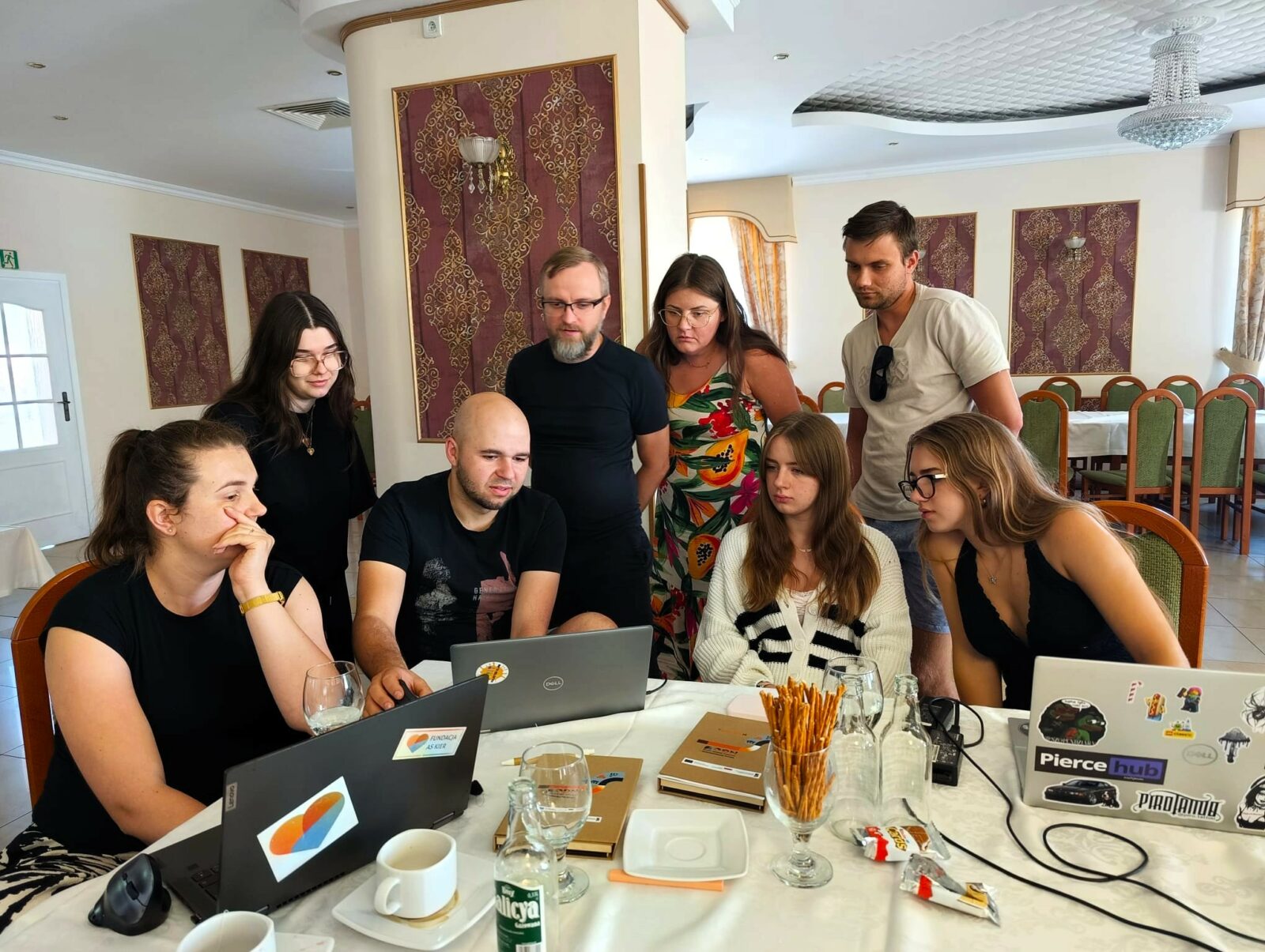 Uczestnicy testują możliwości sztucznej inteligencji - grupa osób stoi przed laptopem i patrzy w ekran